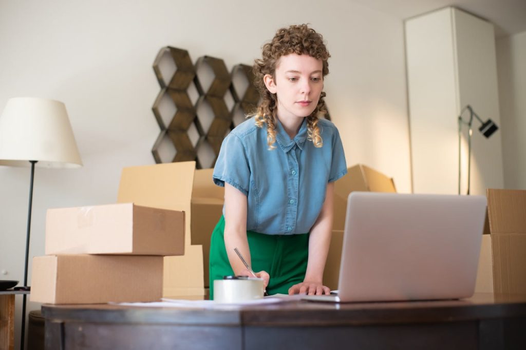Crafting Captivating Headlines: Your awesome post title goes here A young woman working on her laptop surrounded by cardboard boxes, indicating online business operations.
